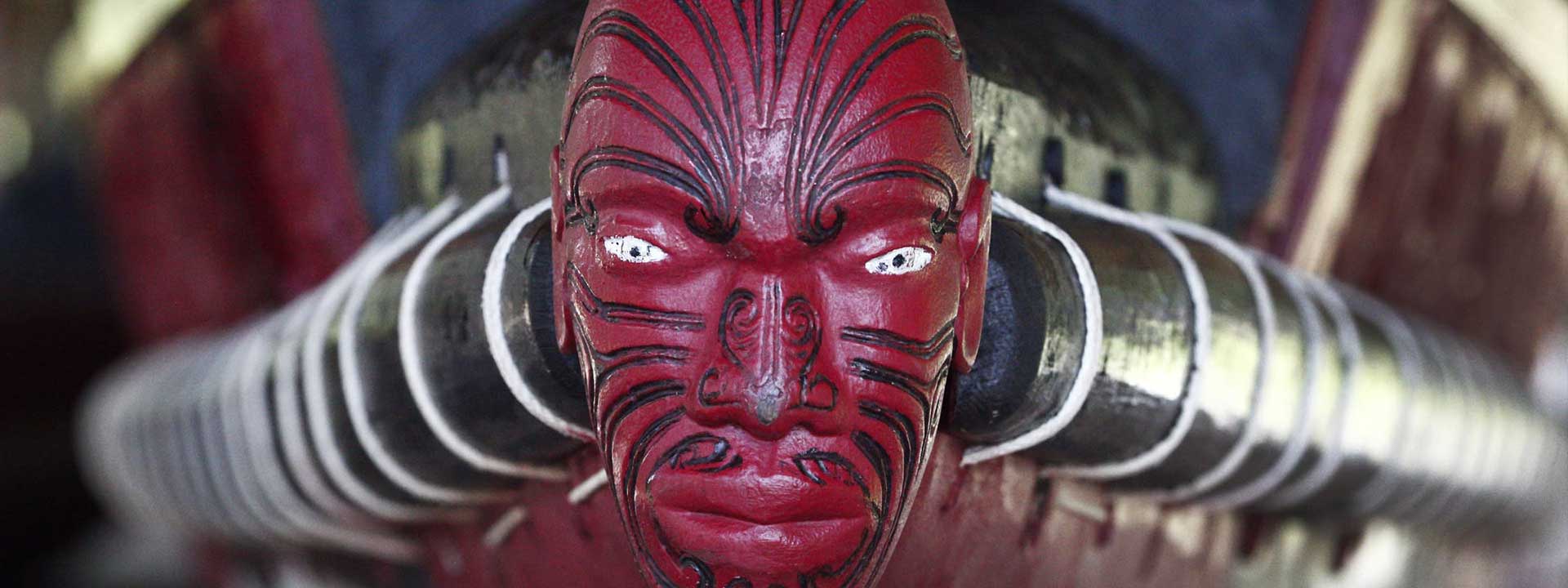 Front of a Maori longboat, carved face painted red with black tattoos. Original photo by Steve Evans.